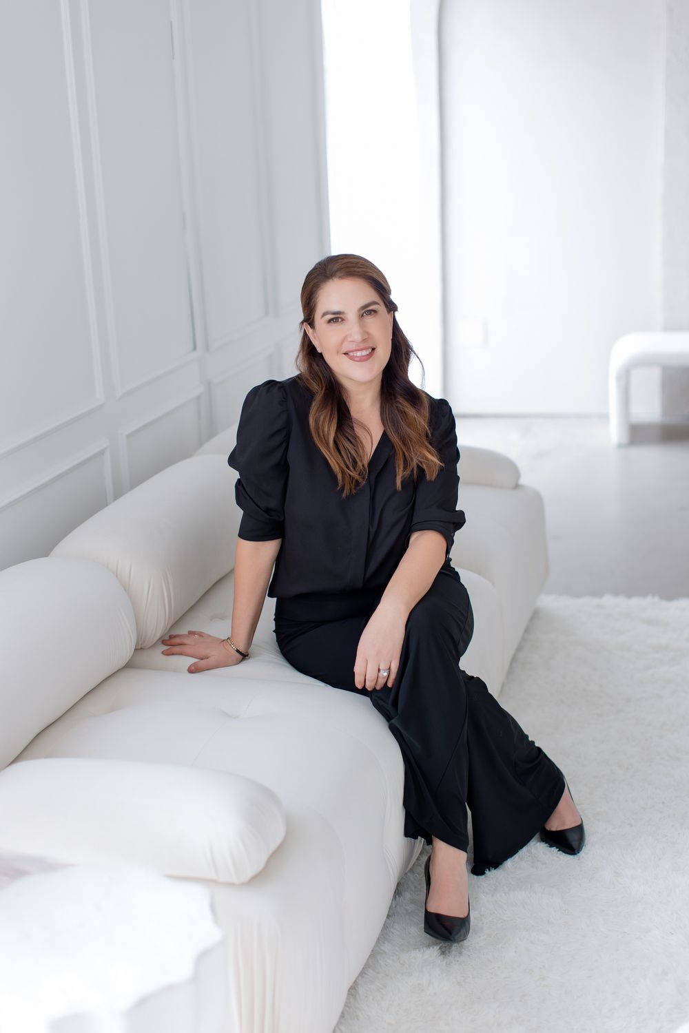 Orange County med spa owner on a white couch with decorative background.