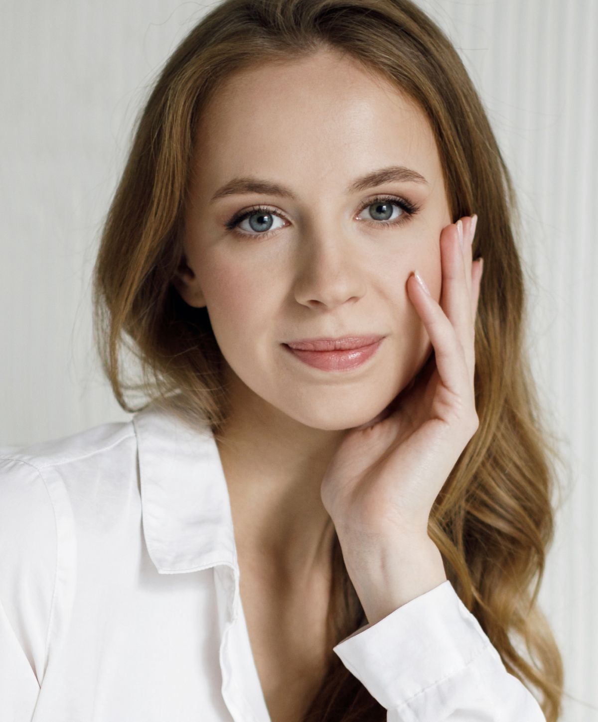 Woman in white shirt, posing thoughtfully with hand.